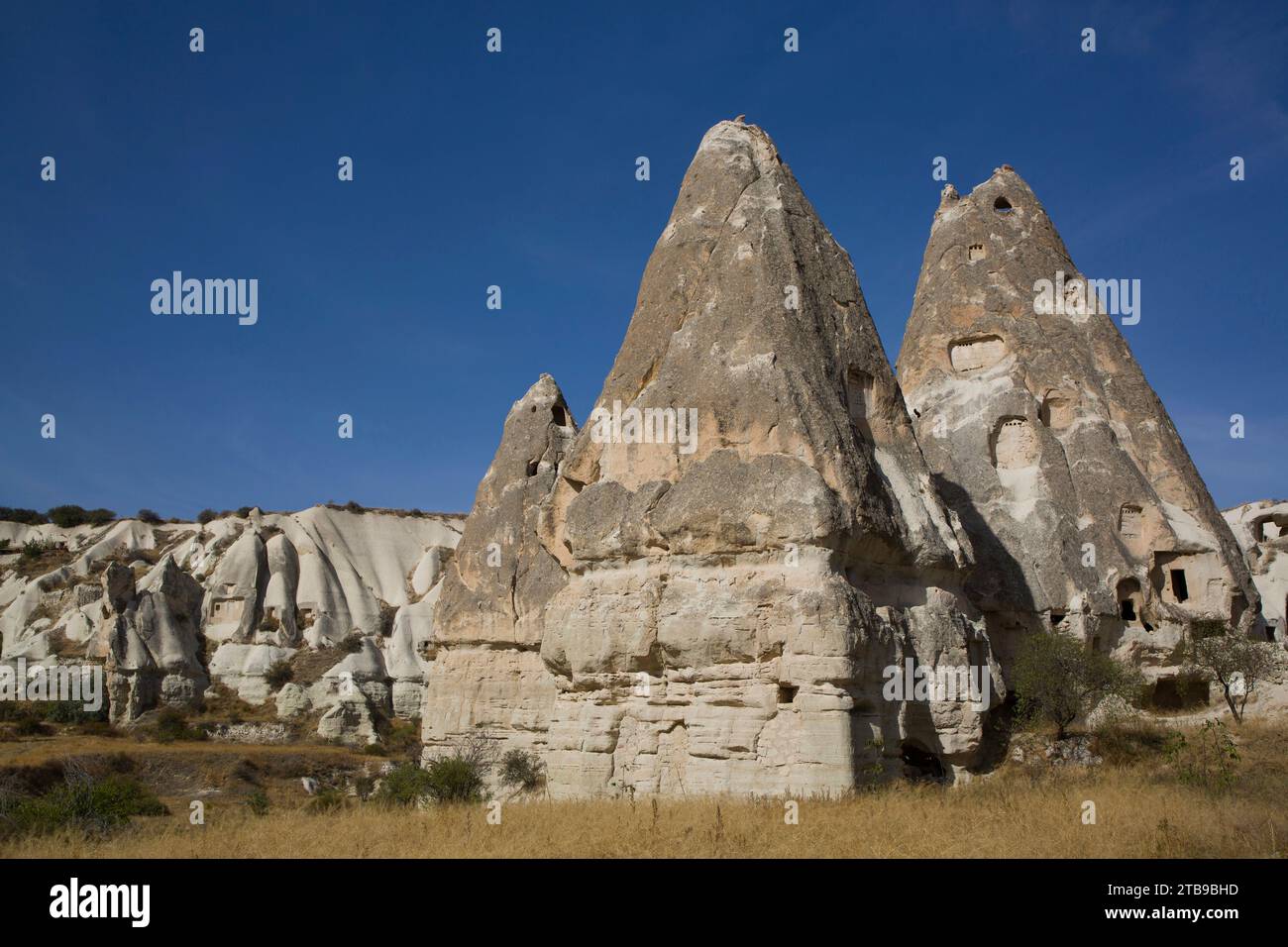 Cave Houses carved out of rock formations against a bright blue sky near the town of Goreme in Pigeon Valley, Cappadocia Region Stock Photo