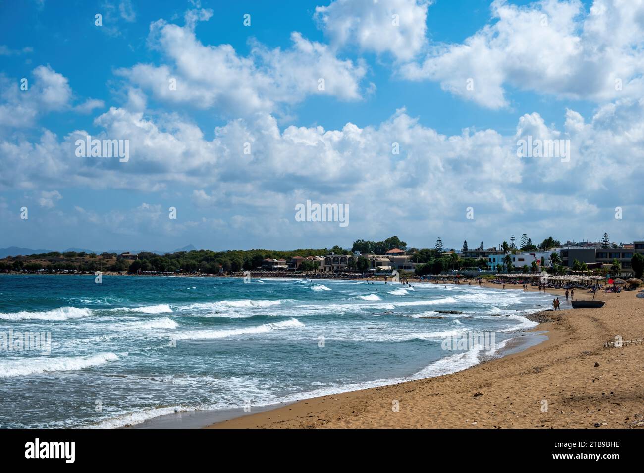 Summer holiday at seaside. Umbrella, lounger, sandy beach sunny day. Ripple sea water, nature, people, swim, leisure, relaxation, sunbathe in Greece. Stock Photo