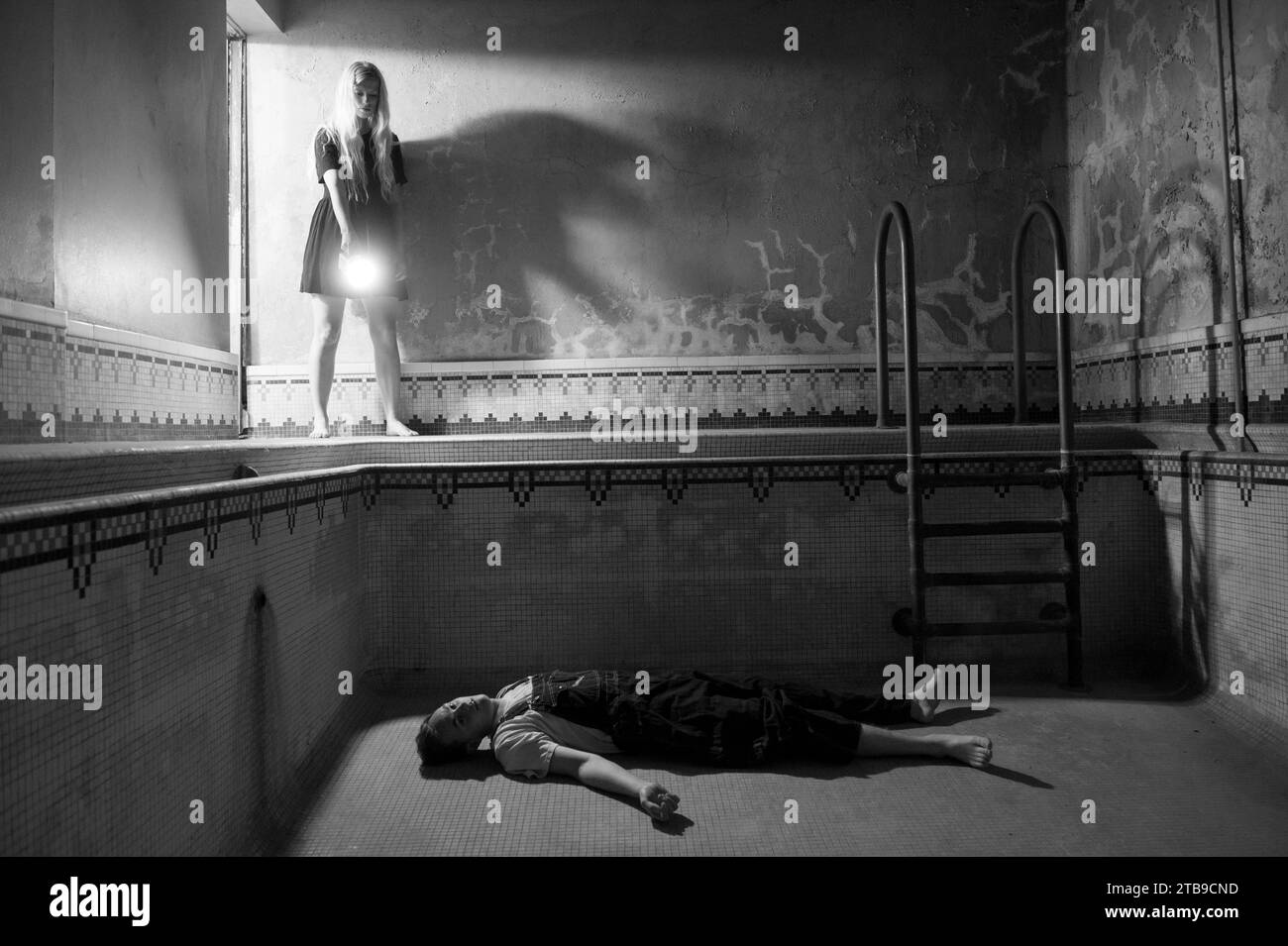 Young man appears to lie dead in an empty swimming pool as a young woman looks on; Lincoln, Nebraska, United States of America Stock Photo