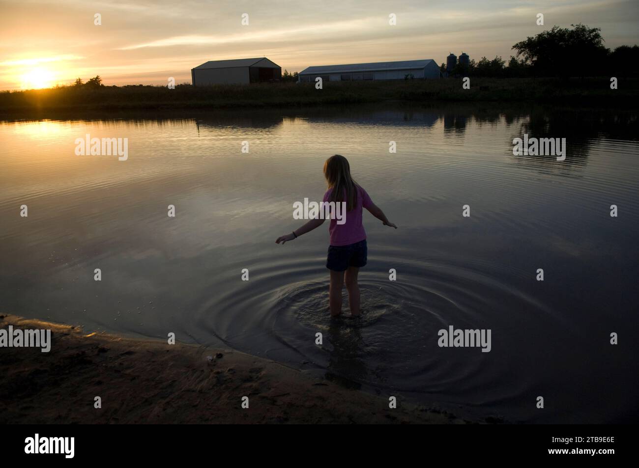 Girl stands in a farm pond at sunset; Greenleaf, Kansas, United States of America Stock Photo