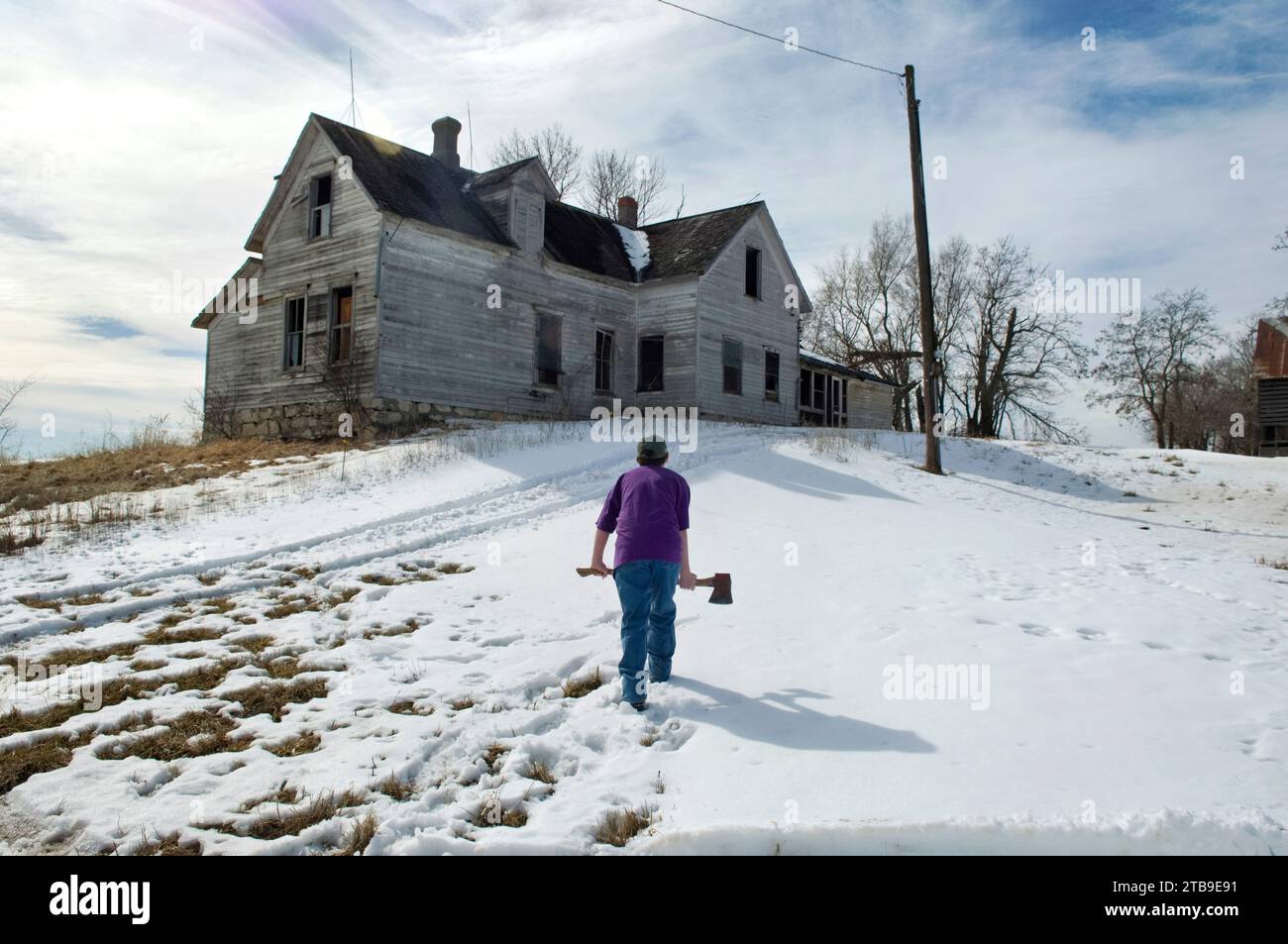 Boy approaches an abandoned farmhouse with an axe; Otoe, Nebraska, United States of America Stock Photo