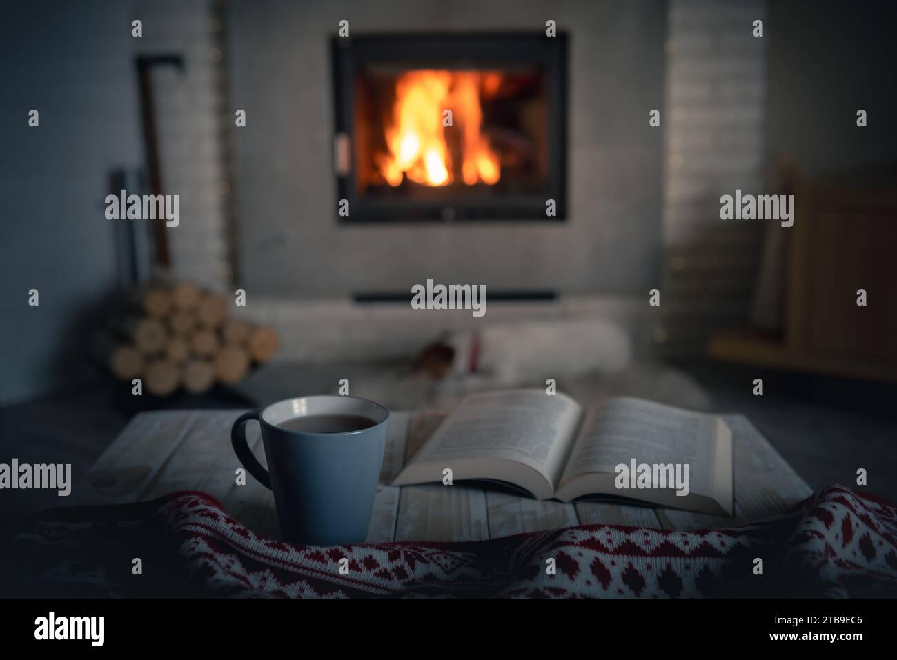 Cozy evening with reading near burning warm fireplace. Book and cup of tea on wooden table. Hygge and home coziness concept Stock Photo