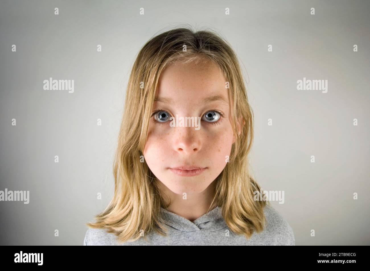 Portrait of a young girl with blond hair and blue eyes against a grey background; Studio Stock Photo