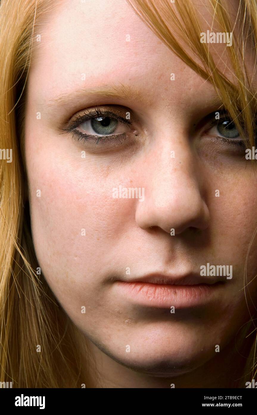 Close-up of a young woman's face, with long strawberry blond hair, blue eyes and a serious expression; Studio Stock Photo