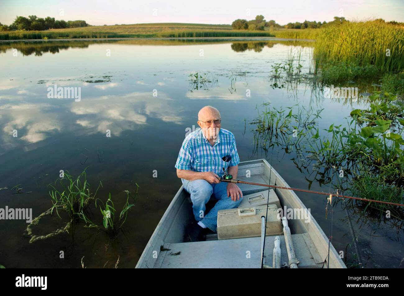 Senior man sits in a rowboat and goes fishing for largemouth bass in a pond; Bennet, Nebraska, United States of America Stock Photo