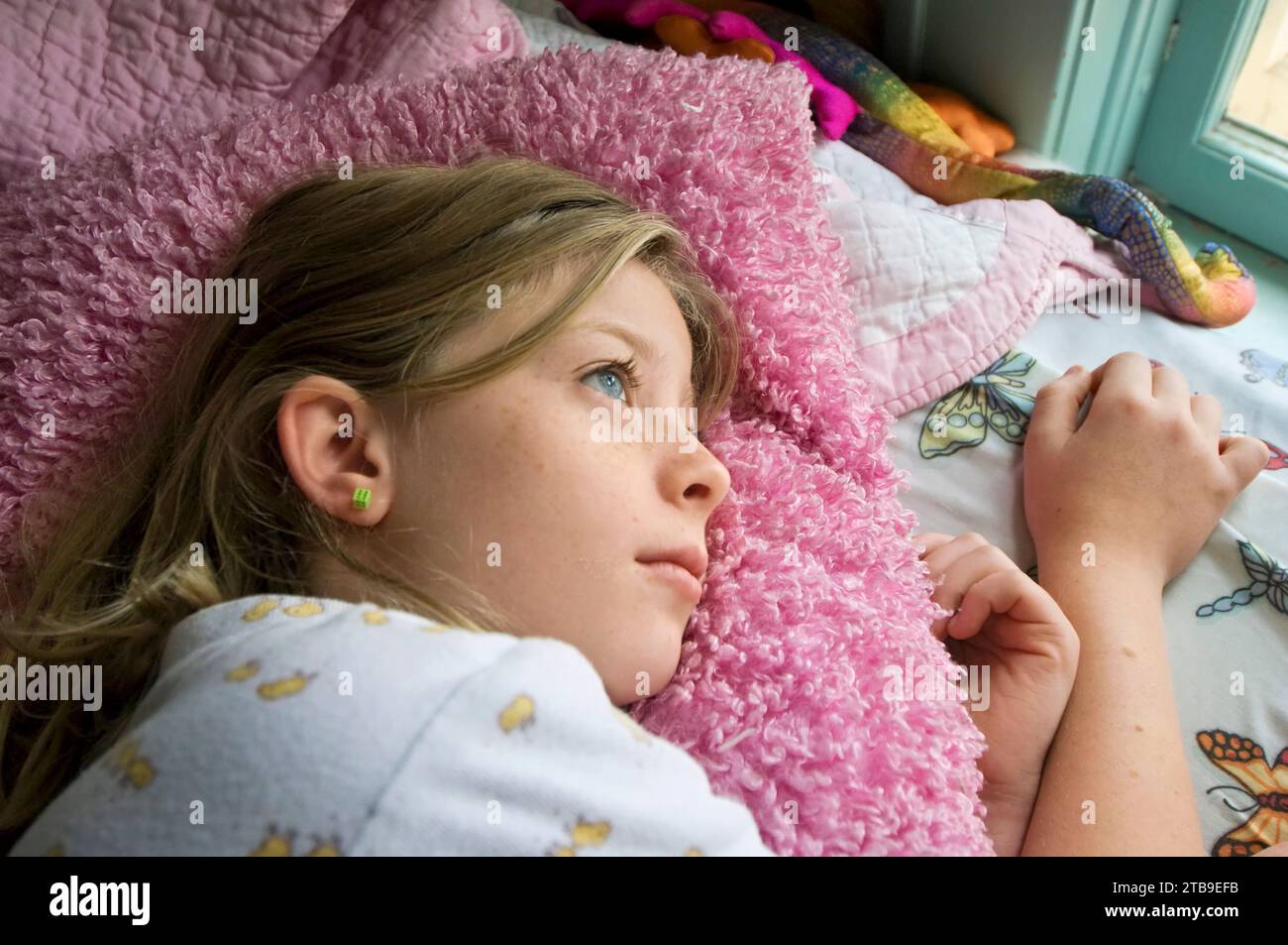 Preteen girl lays in bed looking out the window; Lincoln, Nebraska, United States of America Stock Photo