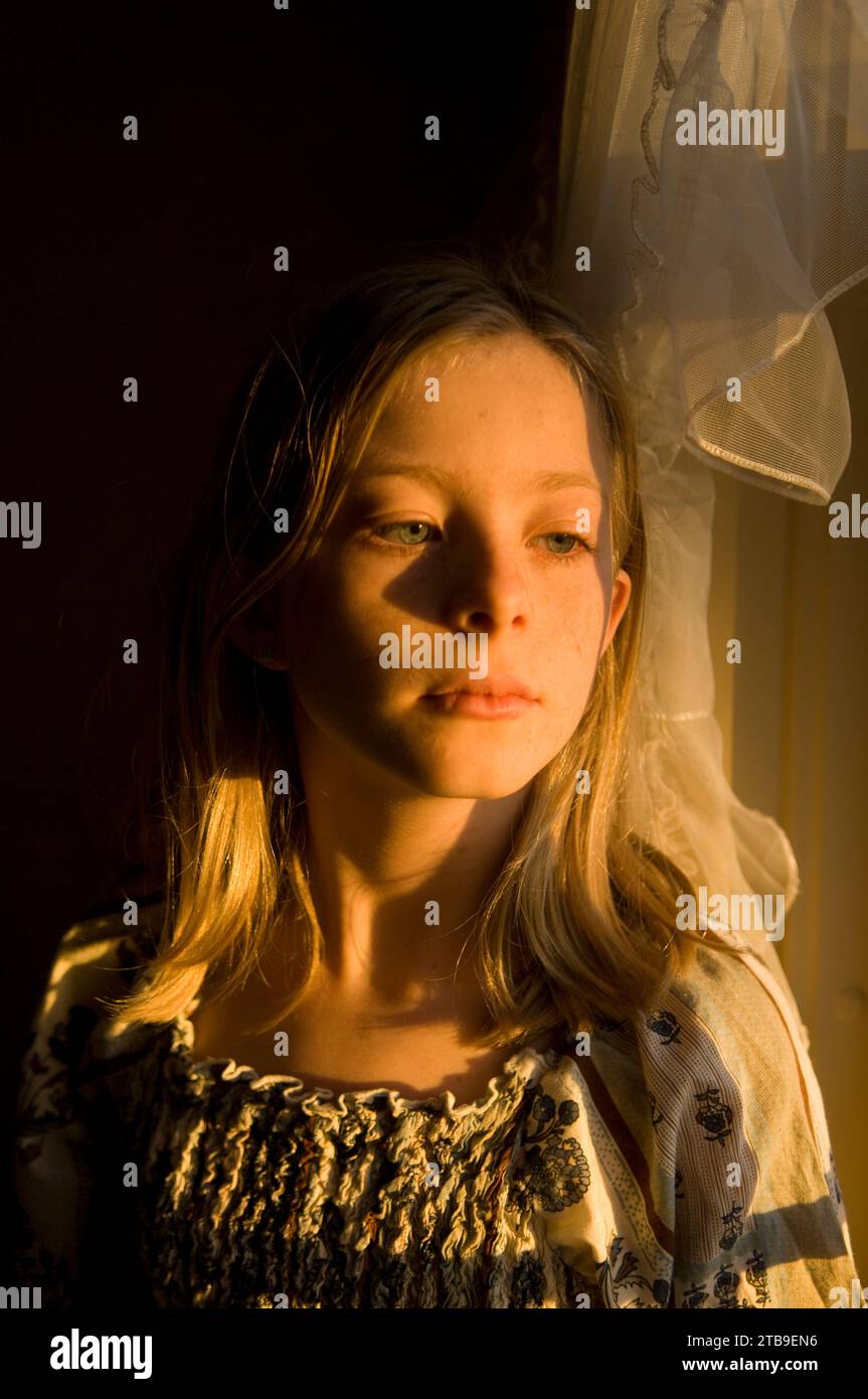 Girl stands in warm sunlight looking out a window; Lincoln, Nebraska, United States of America Stock Photo