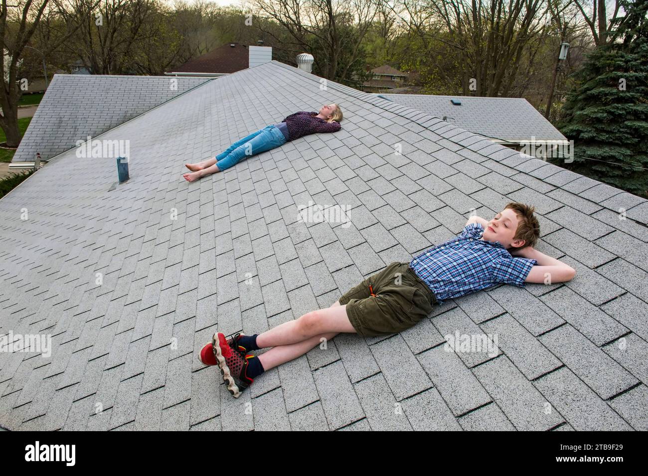 Brother and sister lay on a shingled rooftop; Elkhorn, Nebraska, United States of America Stock Photo