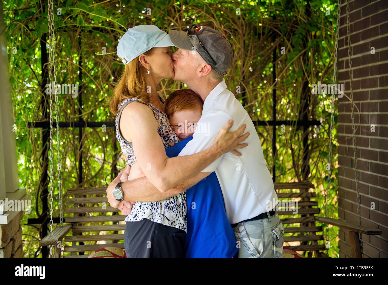 Family of three hug and kiss as they stand on their home porch; Lincoln, Nebraska, United States of America Stock Photo