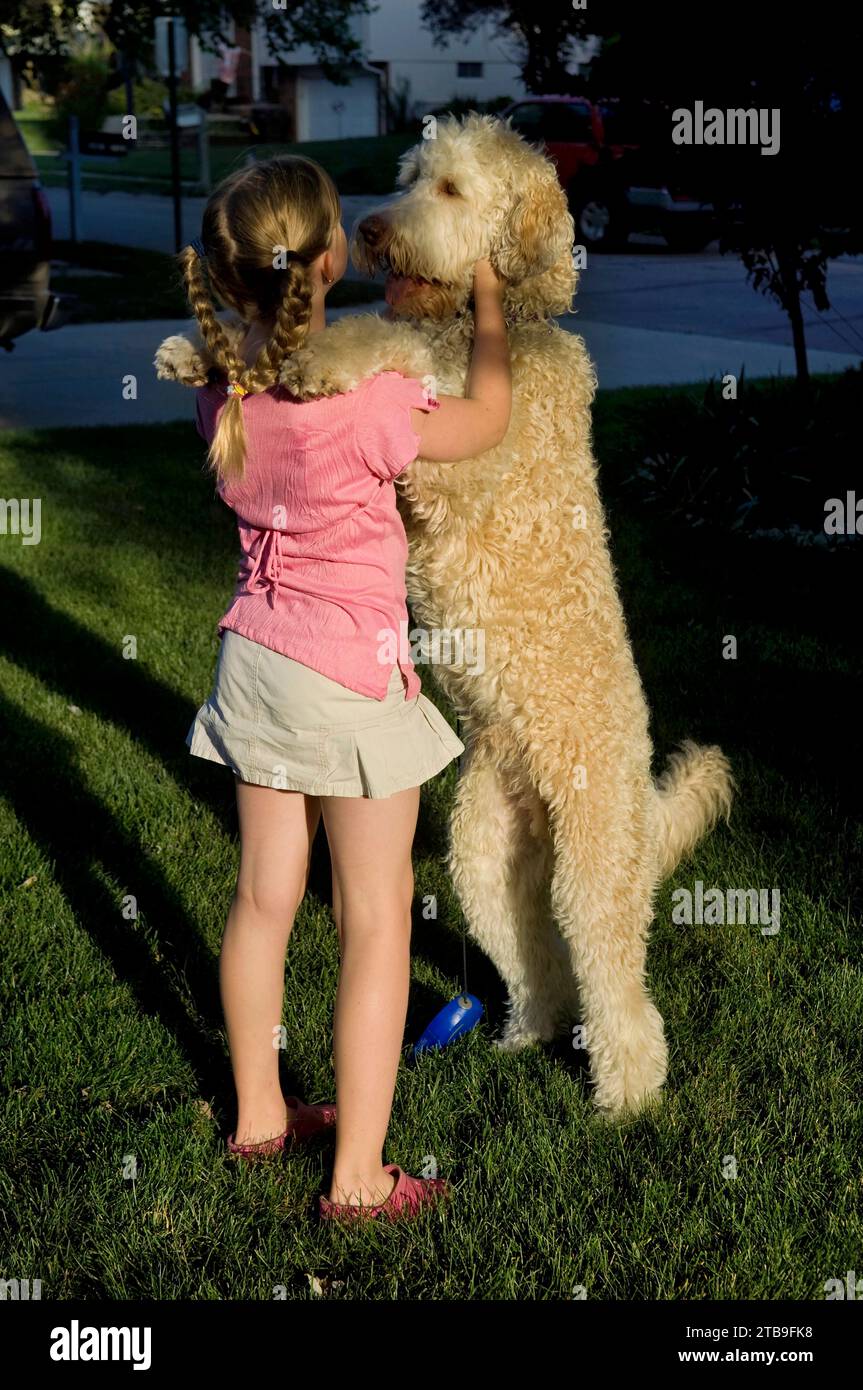Young girl plays with her pet fanci doodle in her yard; Elkhorn, Nebraska, Unied States of America Stock Photo