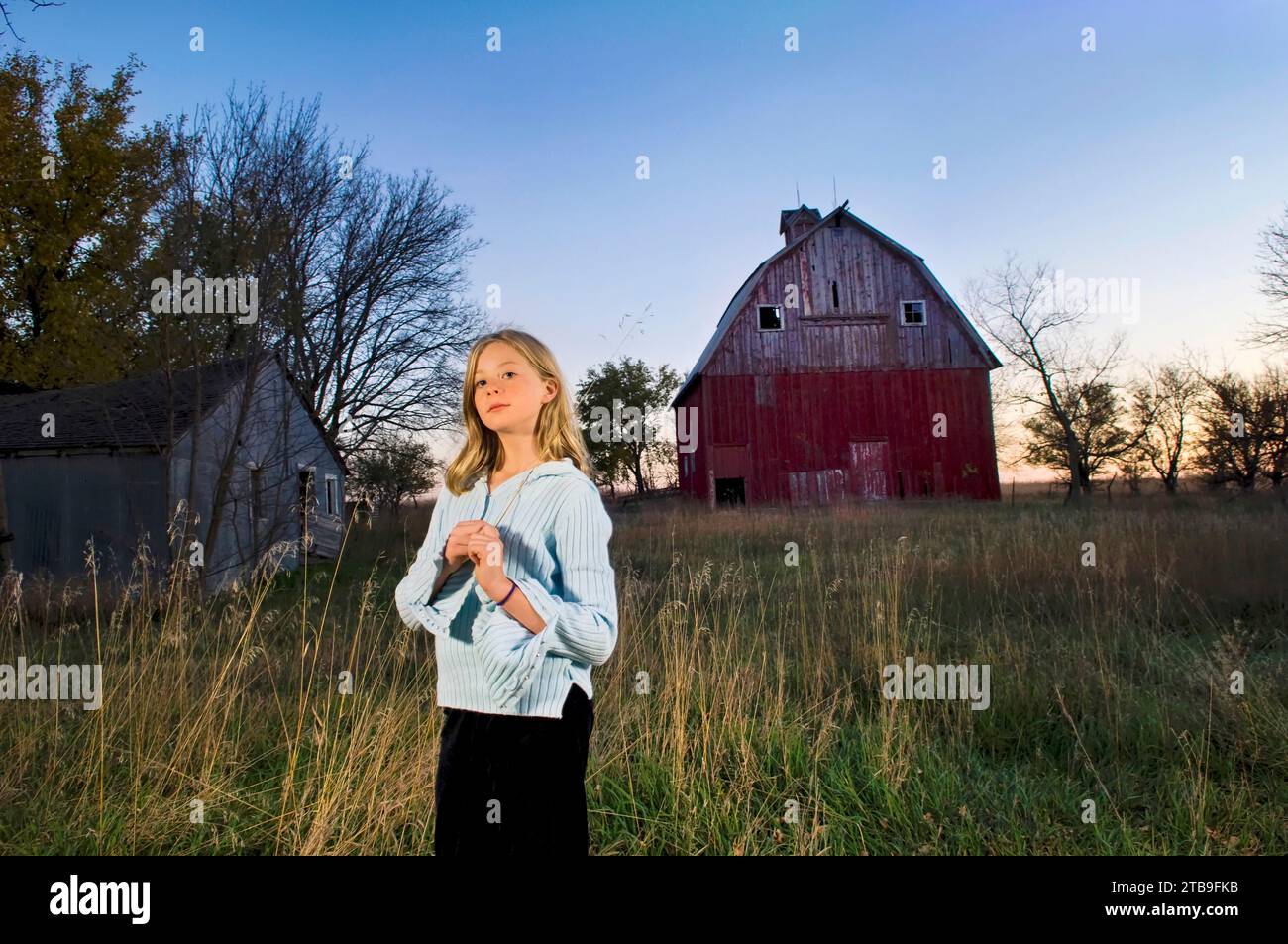 Girl stands for her portrait with a historic barn in the background; Princeton, Nebraska, United States of America Stock Photo