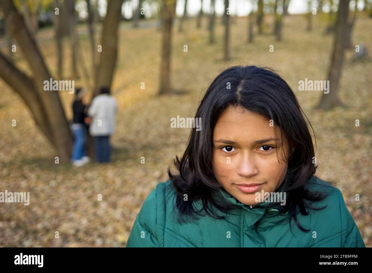 Portrait of a preteen girl in a city park in autumn, with her mother and sister in the background; Staten Island, New York, United States of America Stock Photo