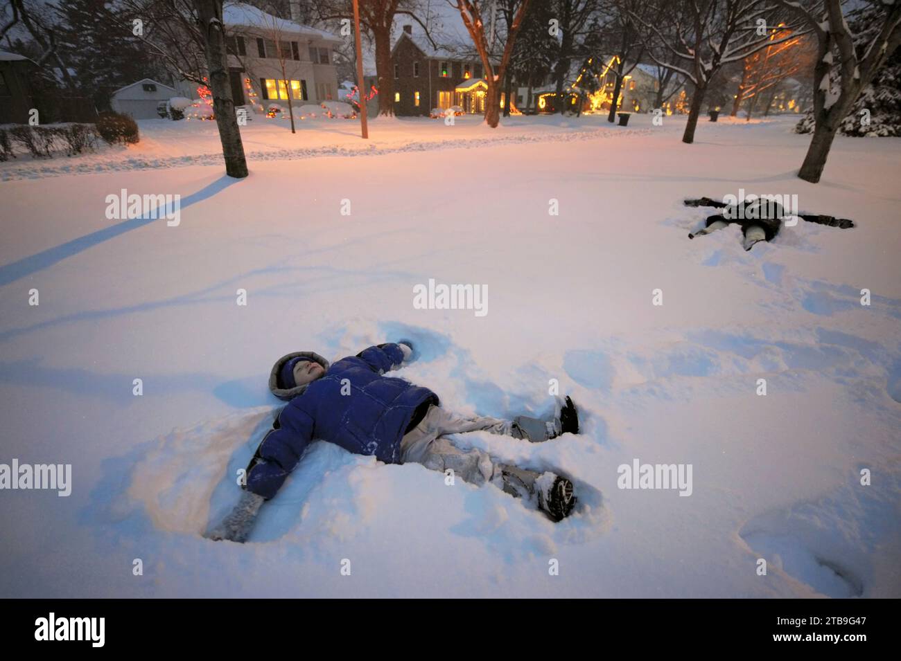 Two siblings make snow angels in their front yard; Lincoln, Nebraska, United States of America Stock Photo