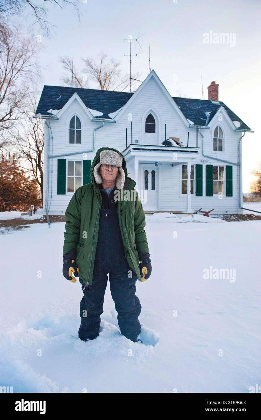 Man in winter wear stands in the snow at a farmhouse; Dunbar, Nebraska, United States of America Stock Photo
