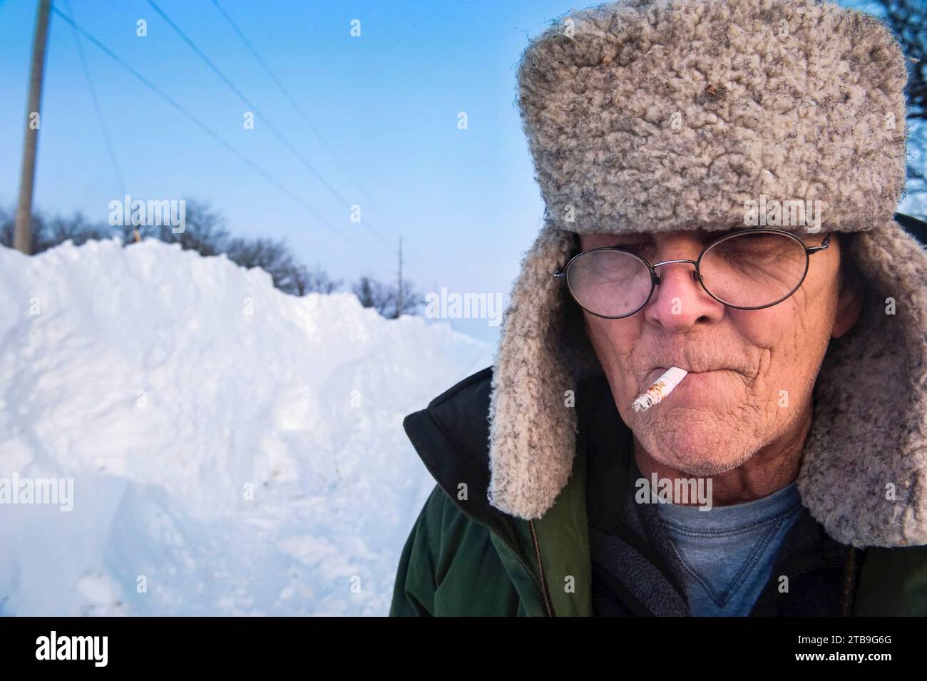 Man smoking a cigarette stands in the snow; Dunbar, Nebraska, United States of America Stock Photo