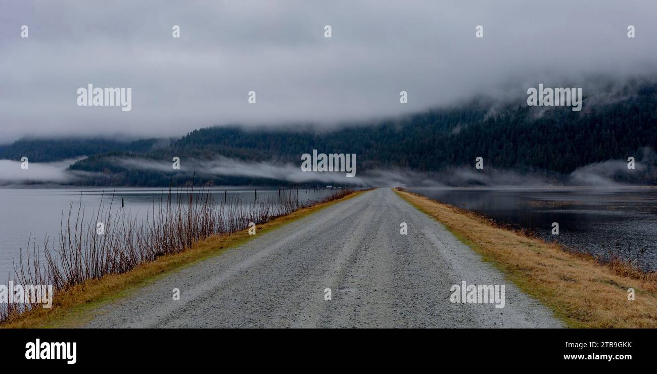 Breathtaking view of walking along the gravel road dyke at Pitt Lake in Maple Ridge on a grey, foggy day; Maple Ridge, British Columbia, Canada Stock Photo