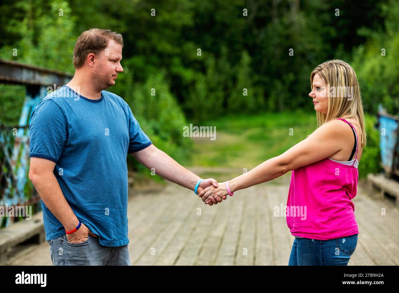 Portrait of a couple standing on a wooden trestle bridge holding hands ...
