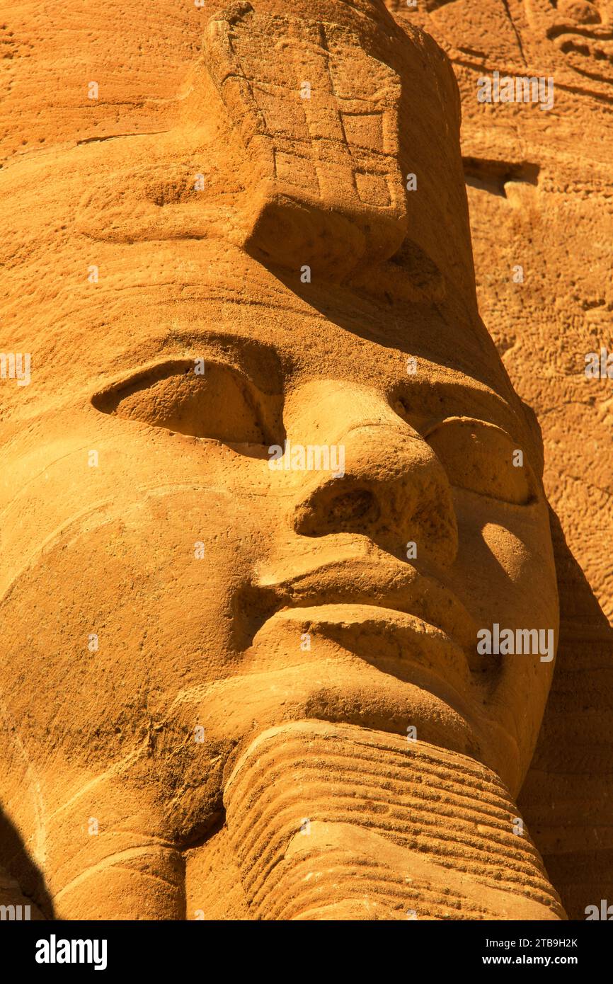 Close-up of one of the Ramses II statues carved out of the mountainside at the front of the Great Sun Temple of Abu Simbel with golden light Stock Photo