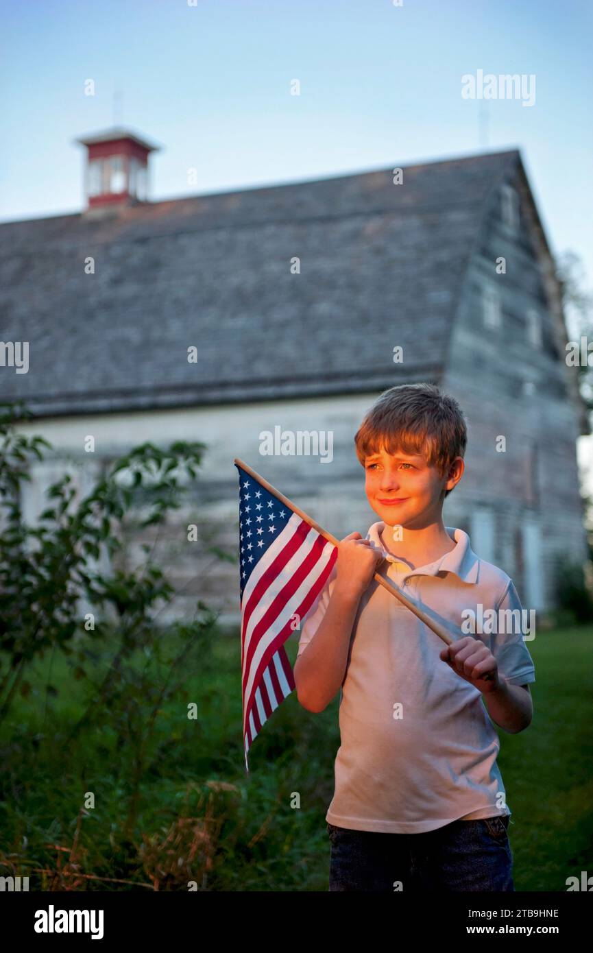 Young, patriotic boy holds up an American flag with an old barn in the background; Lincoln, Nebraska, United States of America Stock Photo