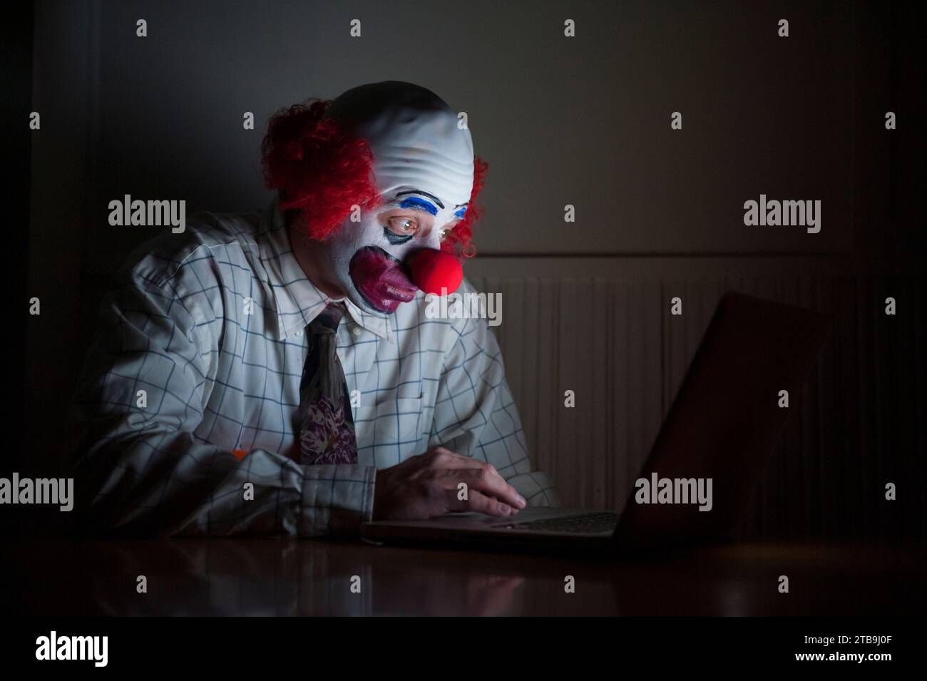 Clown wearing a shirt and tie uses a laptop computer to surf the web, having a wide-eyed look of surprise on his face Stock Photo