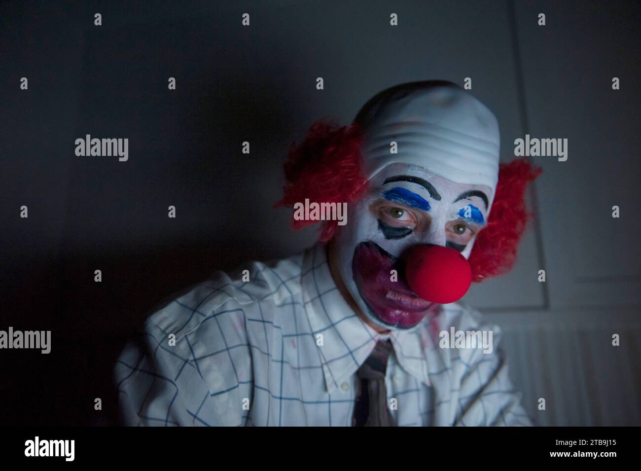 Close-up portrait of a clown sitting by himself in a dark room wearing a shirt and tie; Lincoln, Nebraska, United States of America Stock Photo