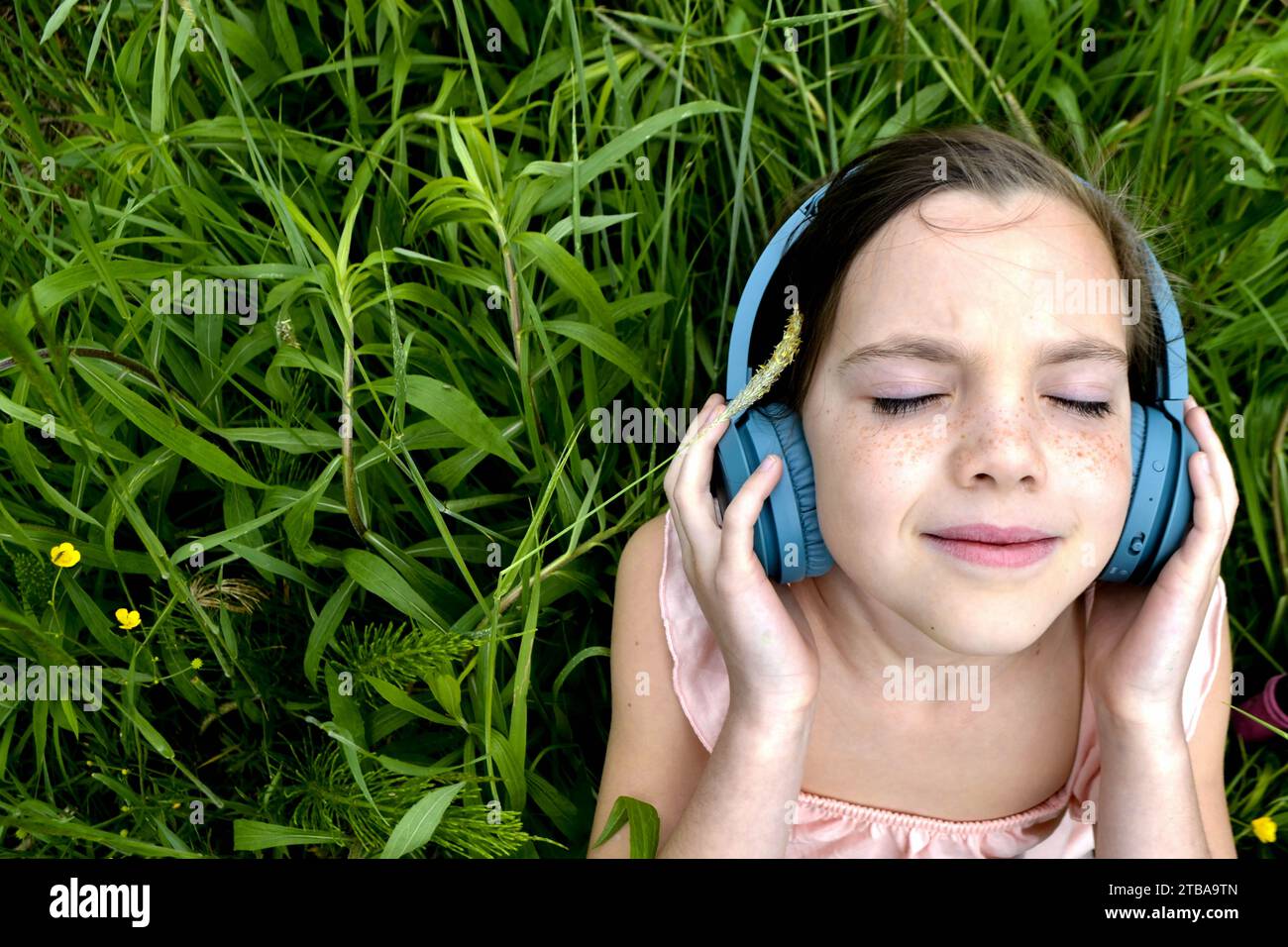 Relaxed woman lying on the grass listening to music with headphones in ...