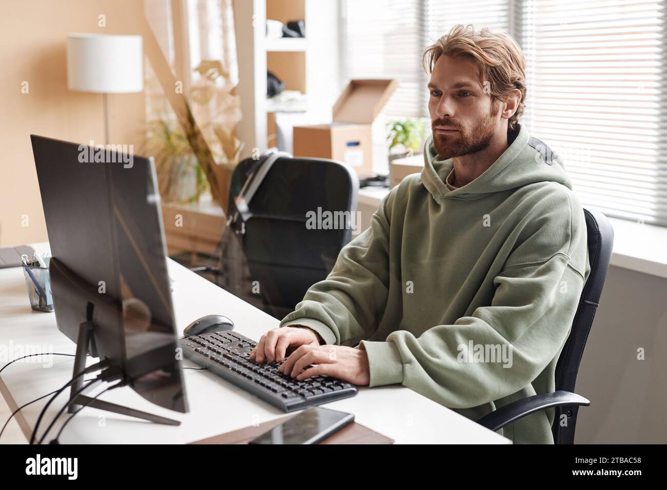 Portrait of young bearded software developer using computer and typing on keyboard while working in office, copy space Stock Photo