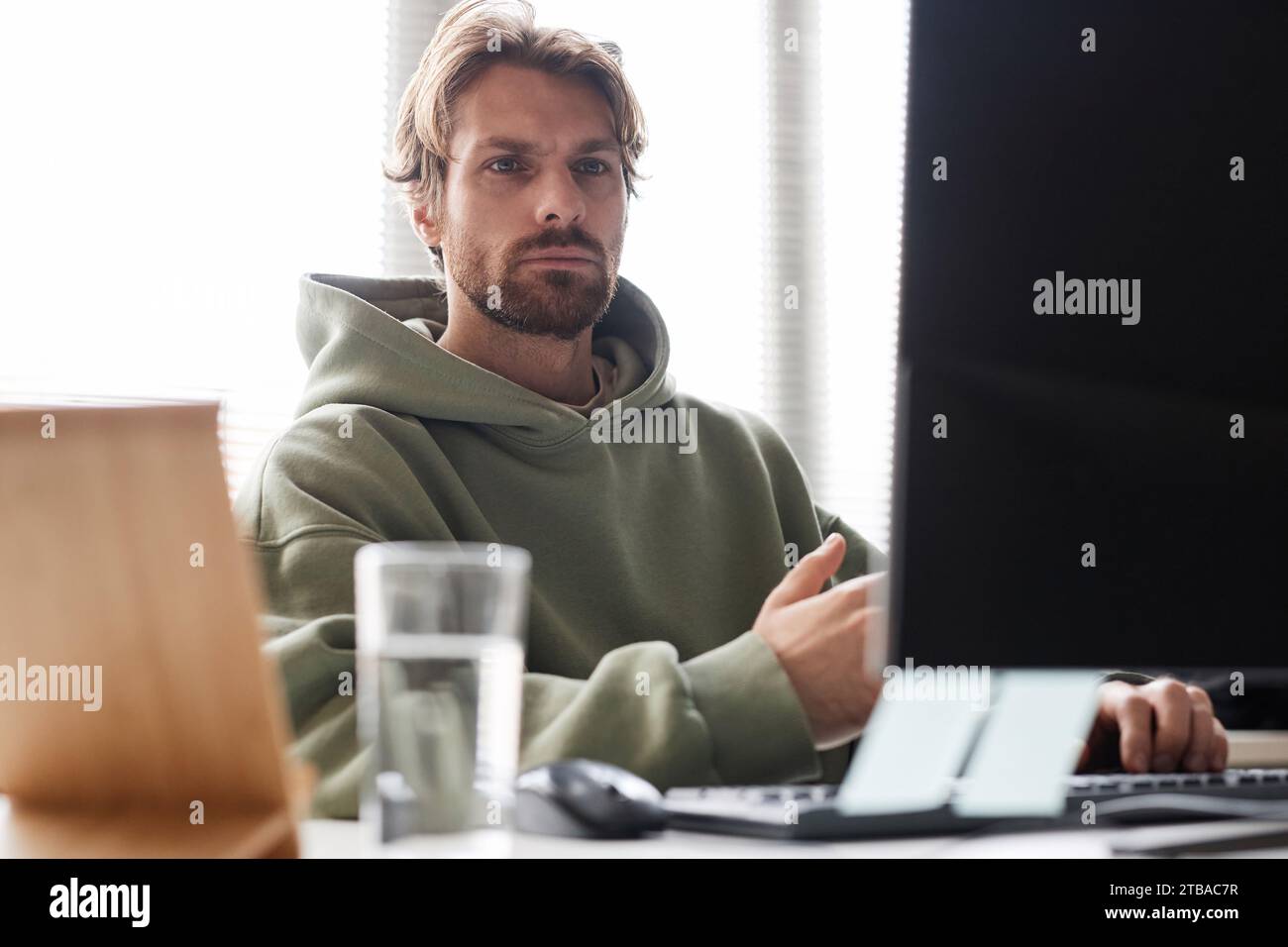 Front view portrait of bearded software programmer looking at computer screen with focused face expression while working in office Stock Photo