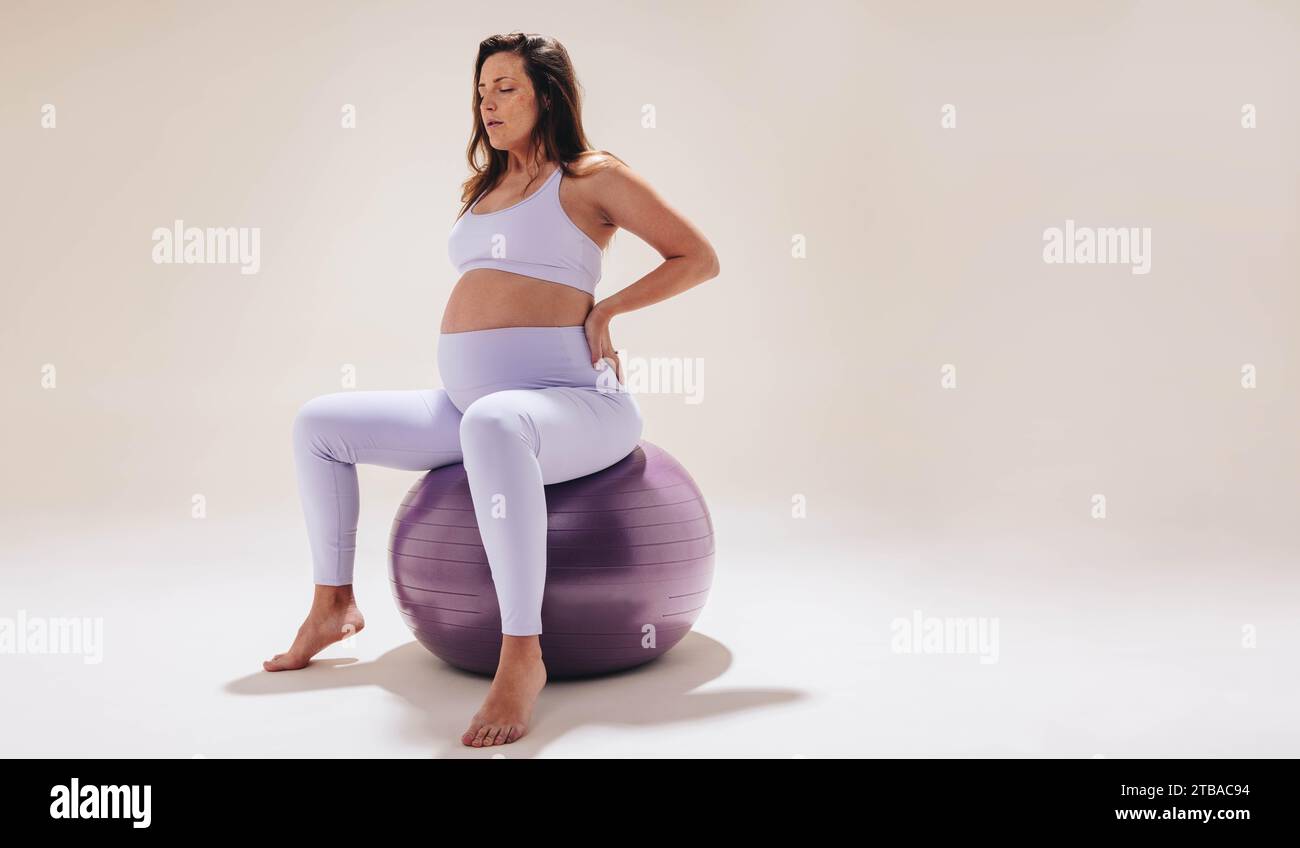 Woman practices prenatal care and self-care during pregnancy. Engaging in fitness exercises, she utilizes an exercise ball for stability and strength. Stock Photo