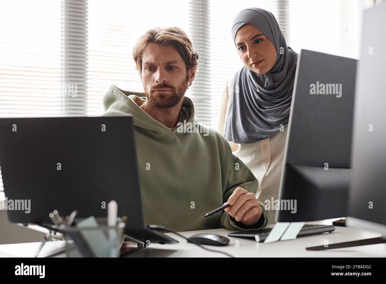 Portrait of IT team with Muslim young woman reviewing project and looking at computer screen Stock Photo