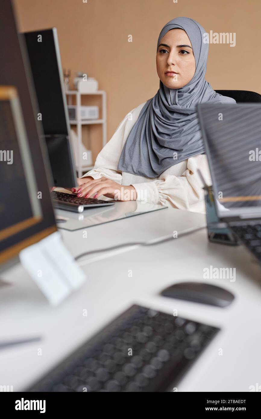 Vertical portrait of young Middle Eastern woman using computer and writing code in IT development office Stock Photo