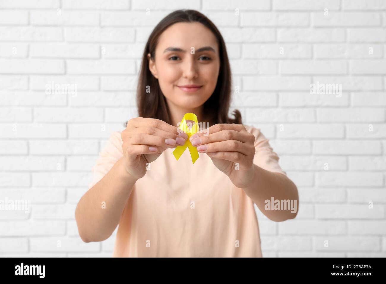 Pretty young woman with yellow ribbon on white brick wall background ...