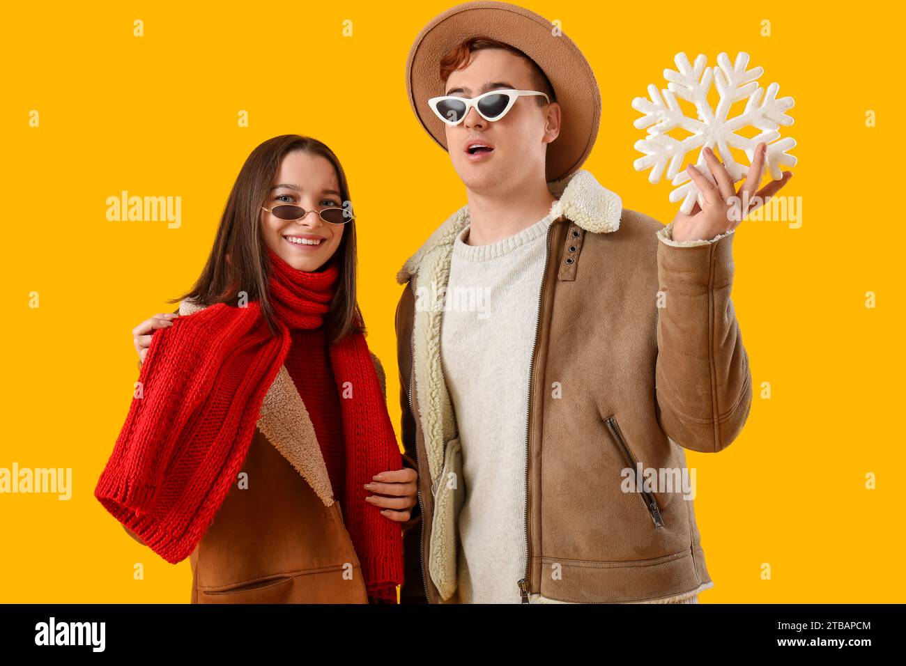 Young couple in winter clothes with snowflake on yellow background Stock Photo