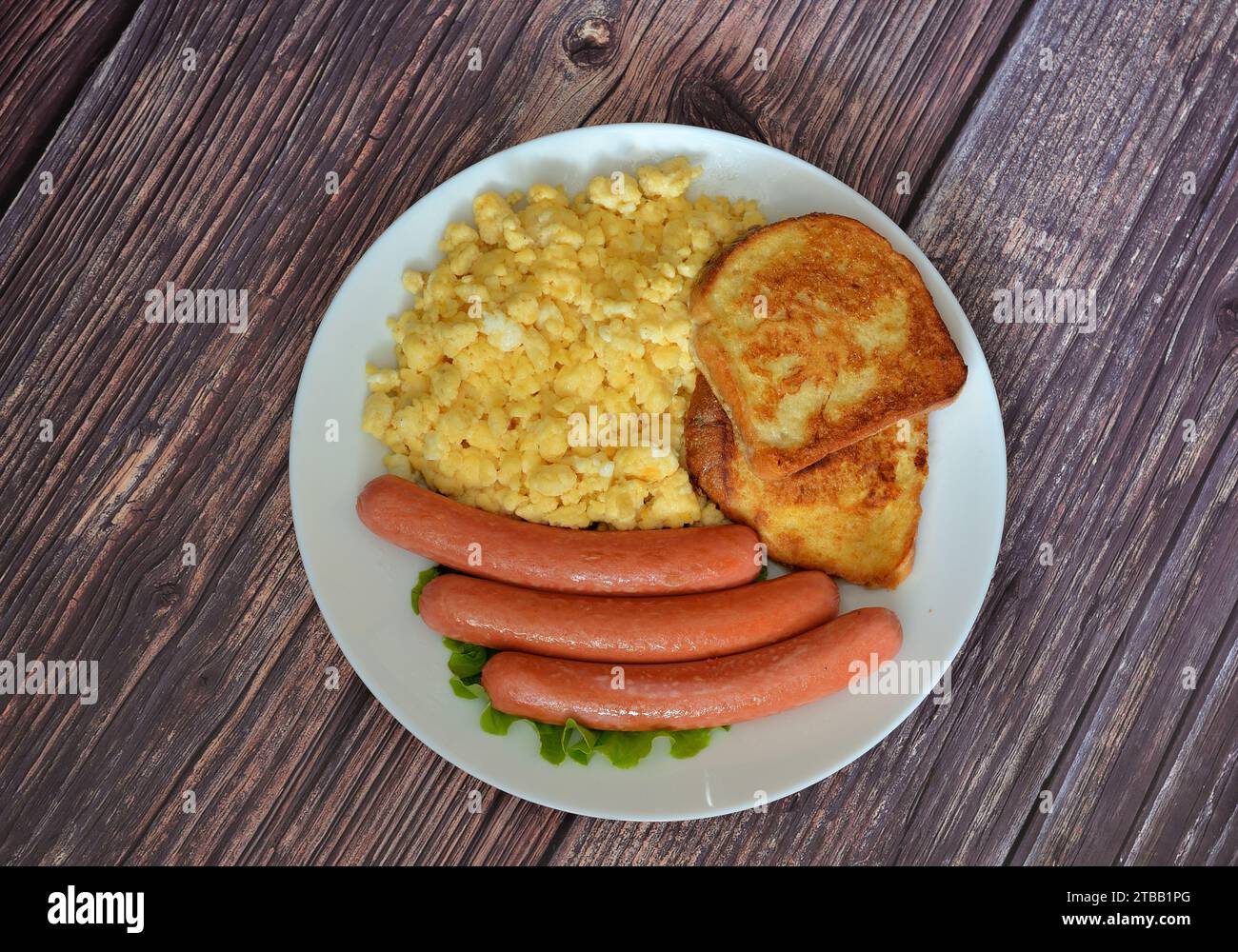 Egg omelet, bread croutons and boiled sausages on a wooden table. Top view, flat lay. Stock Photo
