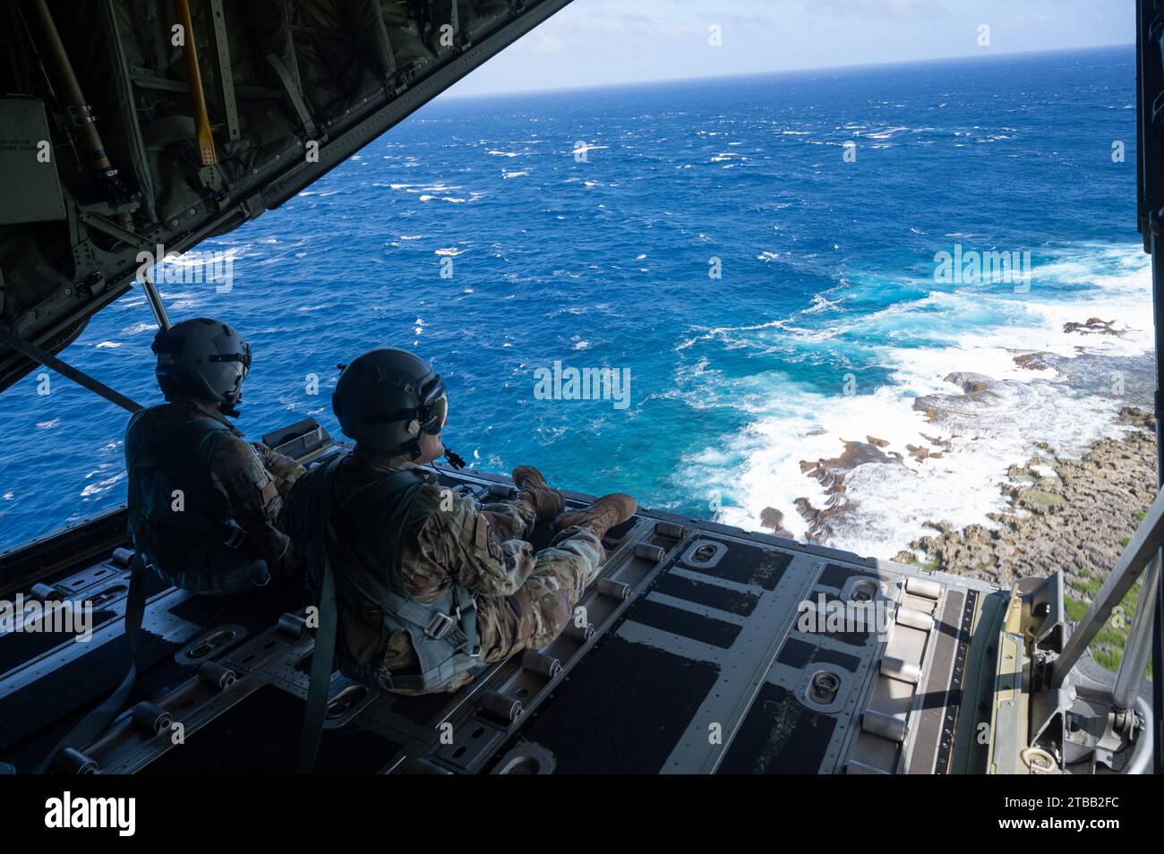 (Left to right) U.S. Air Force Senior Airman John Douglas, 36th Expeditionary Airlift Squadron (EAS) loadmaster, and Senior Airman Ian Munoz, 36th EAS loadmaster, looks out of a C-130J Super Hercules above the Pacific Ocean, Nov. 30, 2023, in support of Operation Christmas Drop 2023 (OCD 23). This event is an opportunity to work together, to learn from one another, and to continue our successful joint efforts in support of humanitarian aid delivery. (U.S. Air Force photo by Senior Airman Brooklyn Golightly) Stock Photo