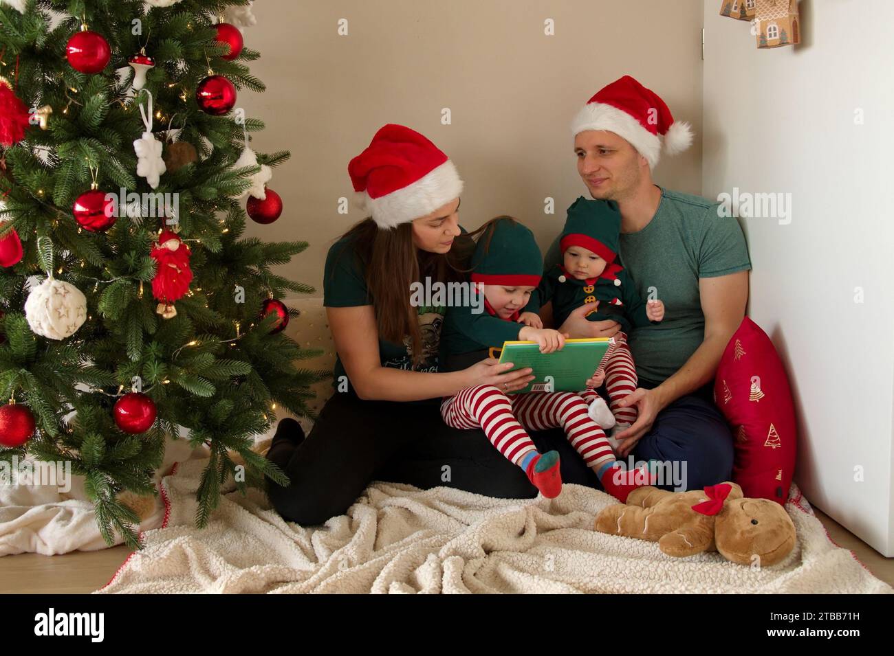 Family with toddler and baby girl sitting in front of Christmas tree Stock Photo