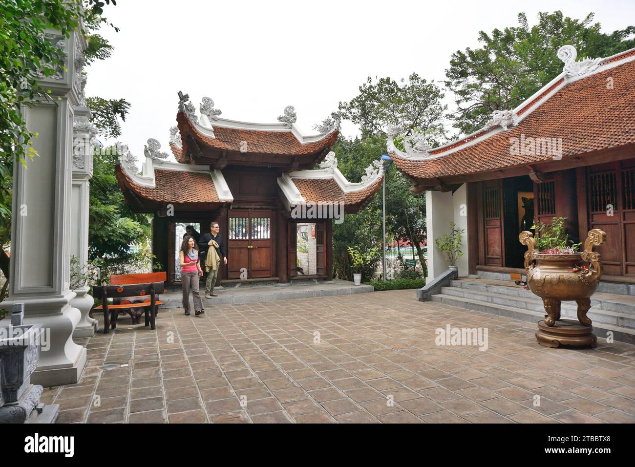 Visitors enter the inner courtyard of a Buddhist temple in Hanoi, Vietnam. The entry gate and temple feature an upswept pagoda-style clay tile roof Stock Photo