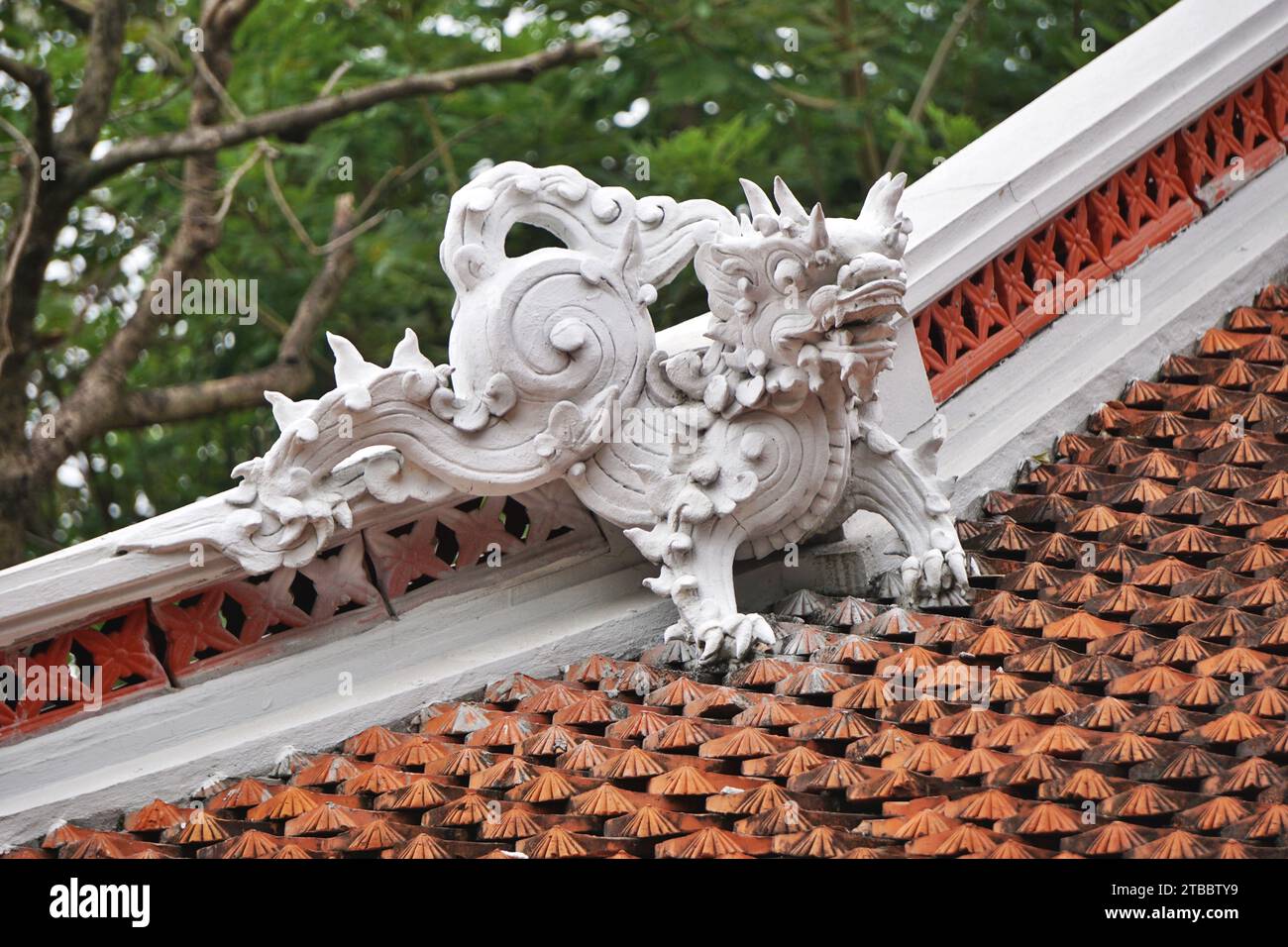 Vintage white dragon sculpture crouches atop a clay tiled roof at a Buddhist temple in Hanoi, Vietnam. Dragon ornaments are a common sight around Asia Stock Photo