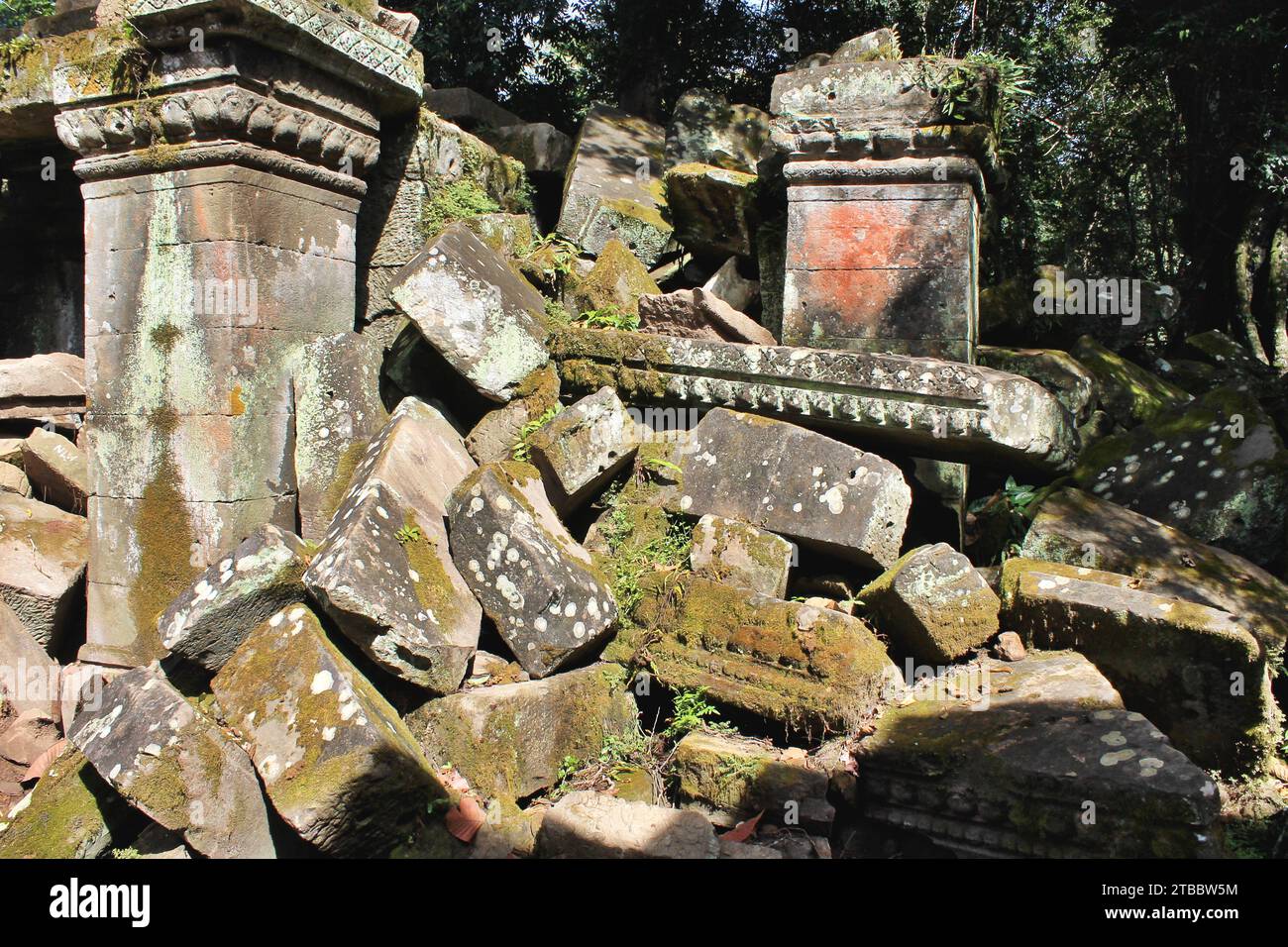 Tumbled down temple stones, some with moss and lichen covered carvings piled among the ancient ruins in Cambodia's Angkor Archaeological Park. Stock Photo