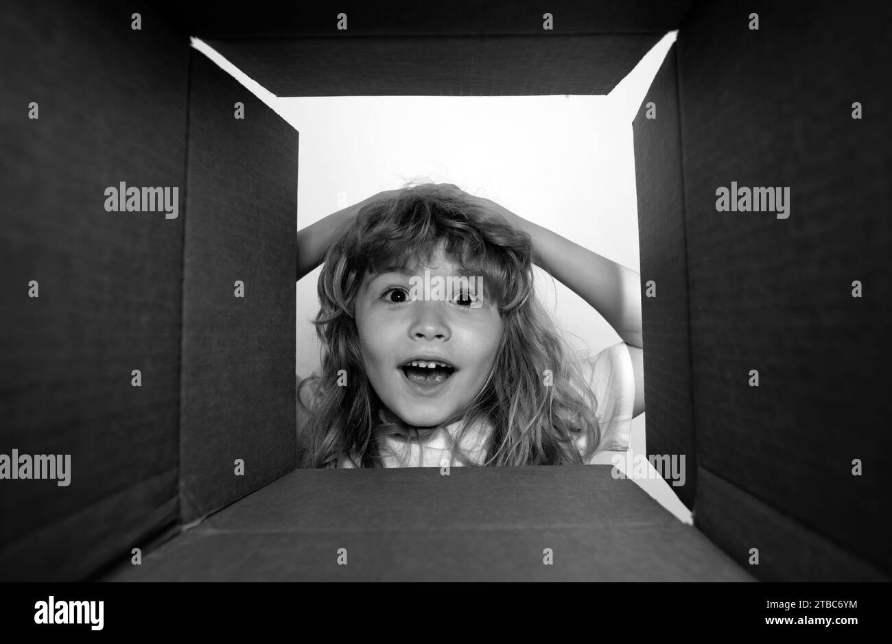 The surprised child unpacking, opening carton box and looking inside. The package, delivery, surprise, kids gift concept. Open box and delivery parcel Stock Photo