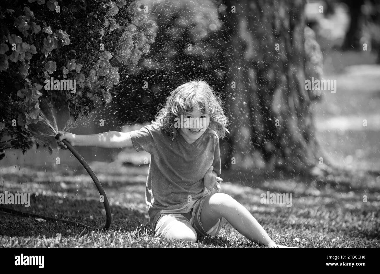 Happy kid boy pours water from a hose. Child watering flowers in garden. Home gardening Stock Photo