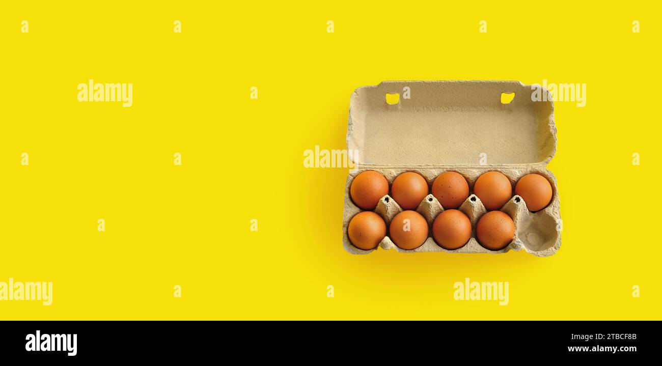 Rustic, organic brown chicken eggs in an open sustainable cardboard tray (box) on a bright, monochrome yellow background. Playful festive image Stock Photo