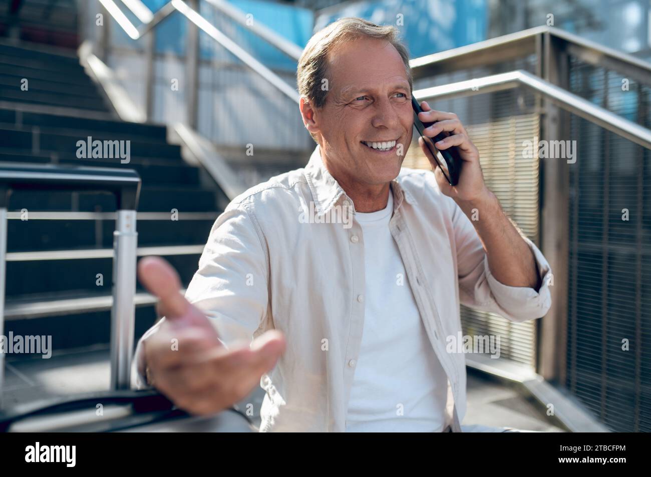 Cheerful man sitting on stairs while talking on the phone. Stock Photo