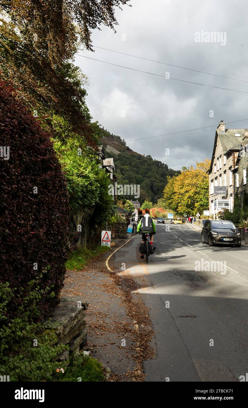 Cyclist pedalling through Glenridding village and shops, Ullswater, Lake District, Cumbria Stock Photo