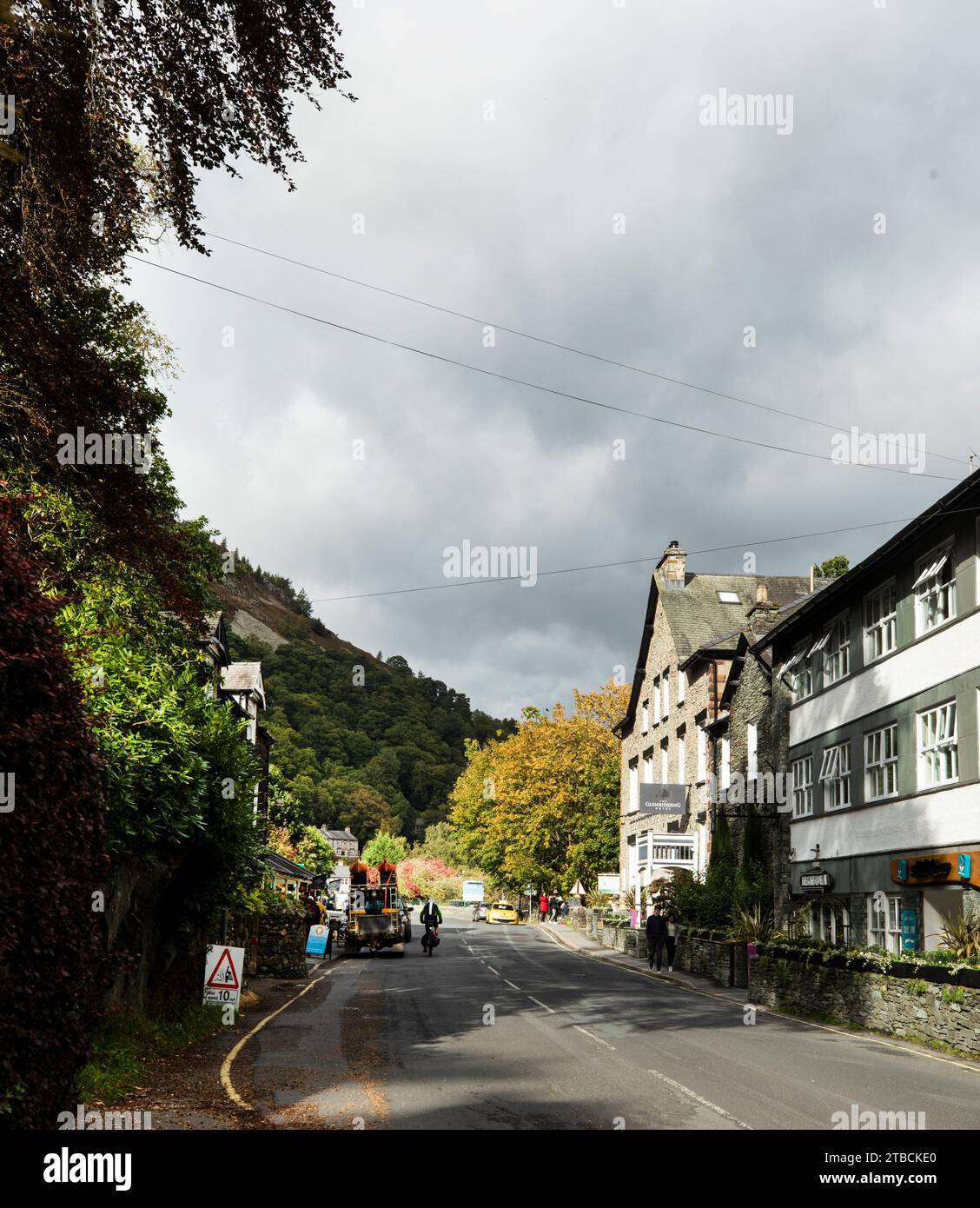 Cyclist pedalling through Glenridding village and shops, Ullswater, Lake District, Cumbria Stock Photo
