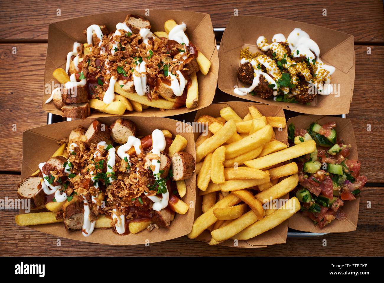 Top view of traditional dish kurry korv and falafel or typical German curry wurst with falafel served on a wooden table and paper plates Stock Photo