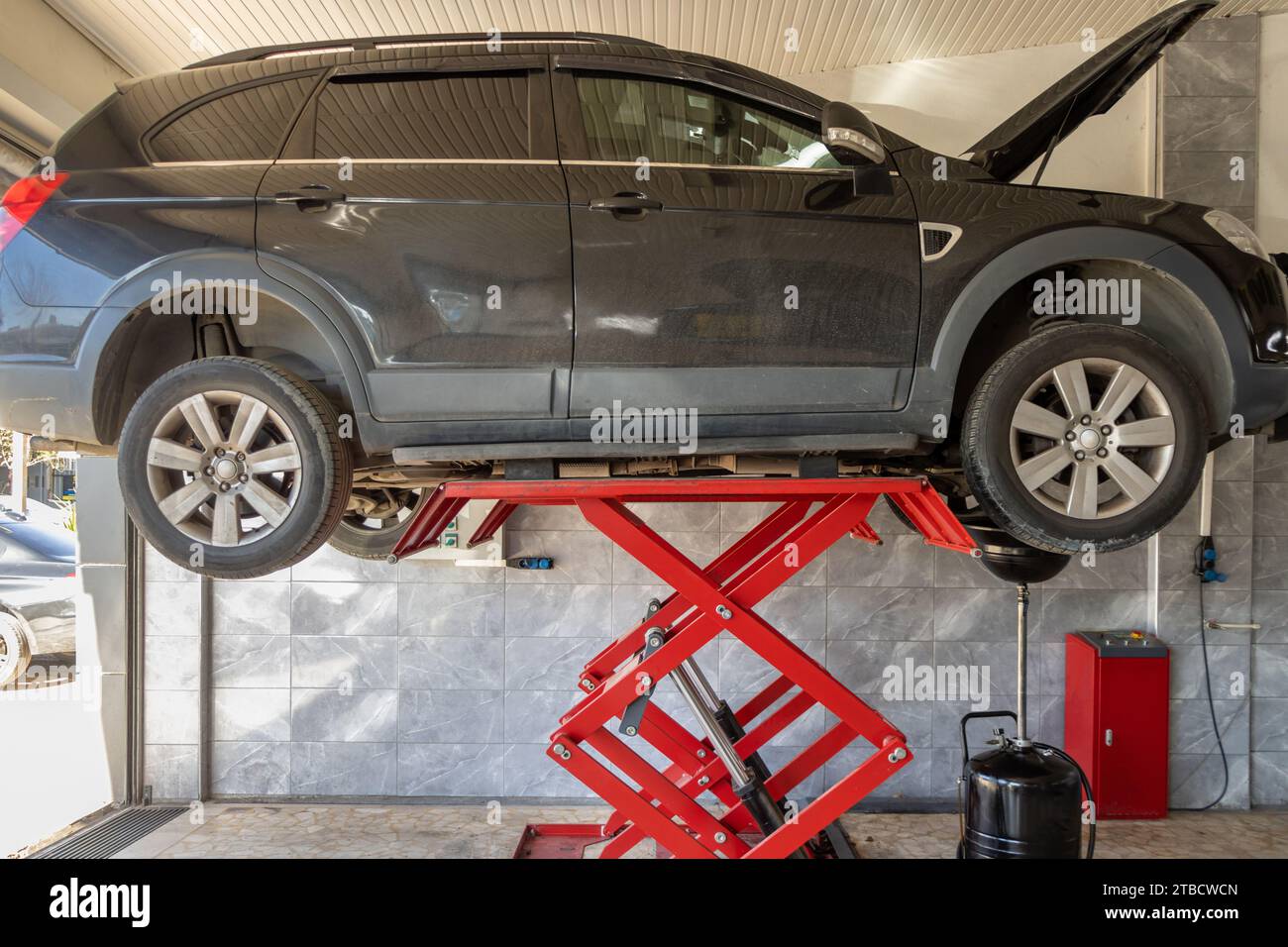 The car, whose repair is completed at the service station, is taken off the lift. Work area with car on high elevator in vehicle repair workshop Stock Photo