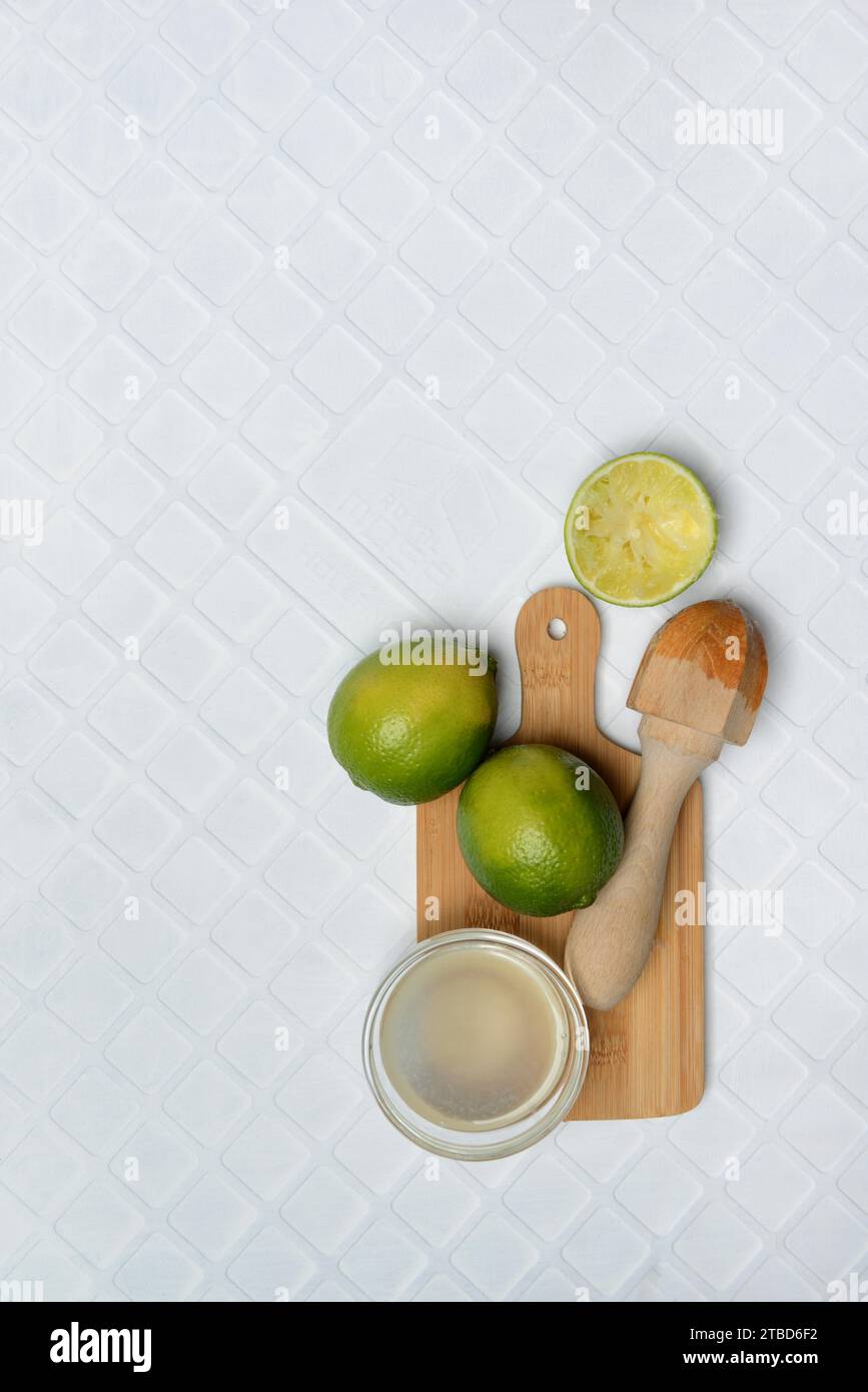 Limes, squeezed, with citrus juicer on chopping board and lime juice in small bowls Stock Photo