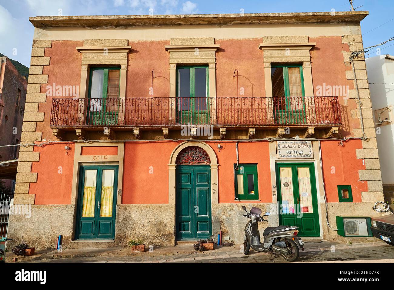 Old house, old rose-coloured facade, green windows and doors, balcony, scooter, Malfa, Salina, Aeolian Islands, Sicily, Italy Stock Photo