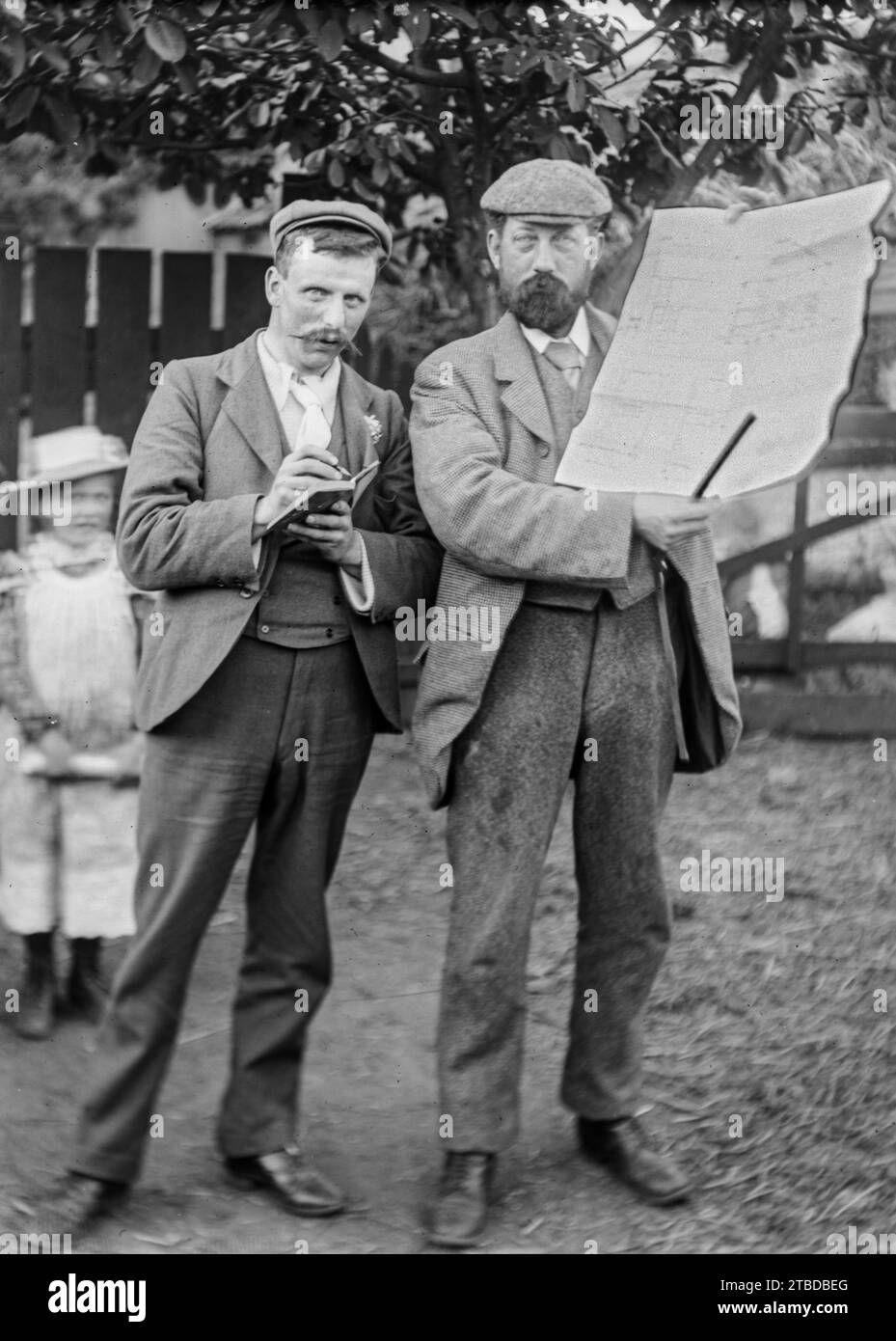 Edwardian casual portrait of two men in suits, outside, one holding up a large plan or diagram and the other with a notebook. Taken from a vintage glass plate negative.  C1900 – 1910 Stock Photo